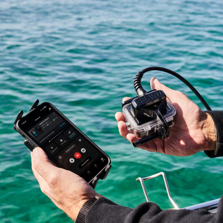 Person holding action camera and phone connected using Seavu Seeker with cable between receiver and transmitter