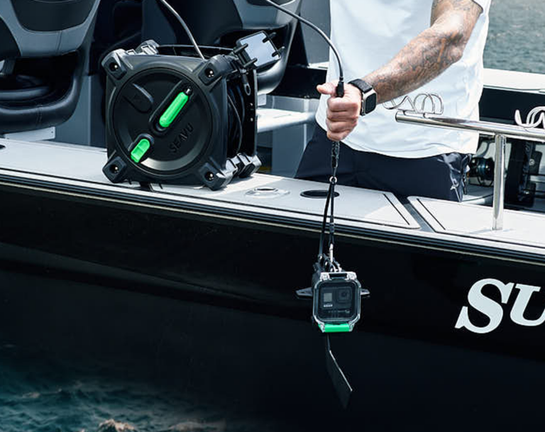 Person deploying Seavu Explorer with Drift Fin from boat, cable reel on deck showing live underwater footage on mobile